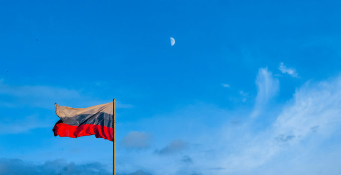Rysslands flagga på en flaggstång med en halvmåne i bakgrunden.