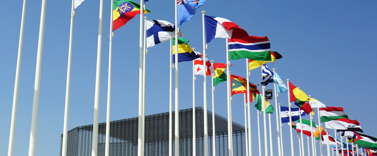A group of flags flying in the air next to a building.