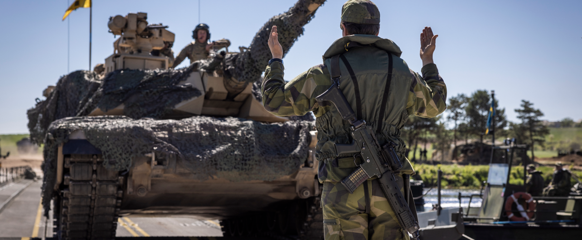 En man i kamouflagekläder som står framför en stridsvagn.