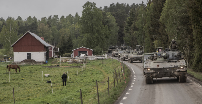 Militärfordon som kör längs en landsväg vid en hästhage.