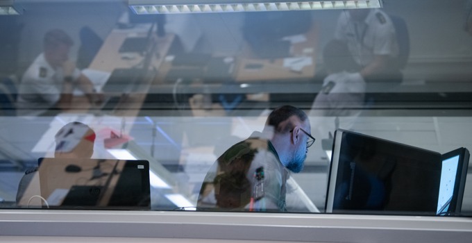 Personer vid datorer bakom en glasruta.