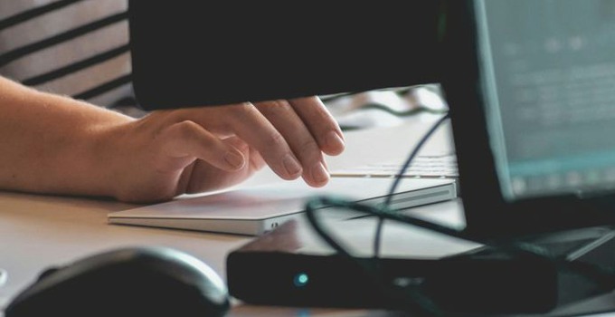 En hand framför en datorskärm.