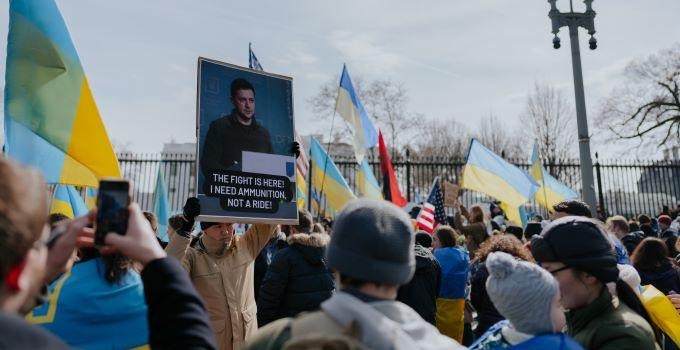 Människor som demonstrerar mot kriget i Ukraina där en person håller upp ett plakat med Zelensyjs foto. 