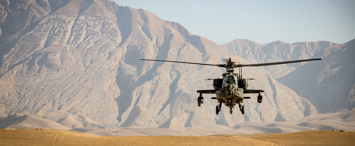 En helikopter som flyger över ett ökenlandskap med berg i bakgrunden.