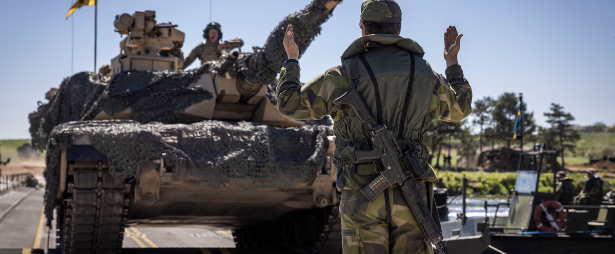A man in camouflage standing in front of a tank.