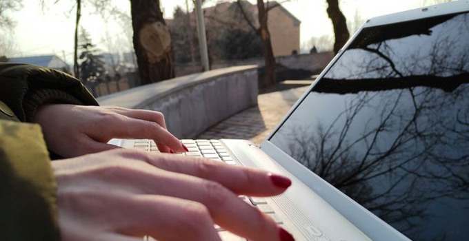 Händer på en laptops tangentbord utomhus.