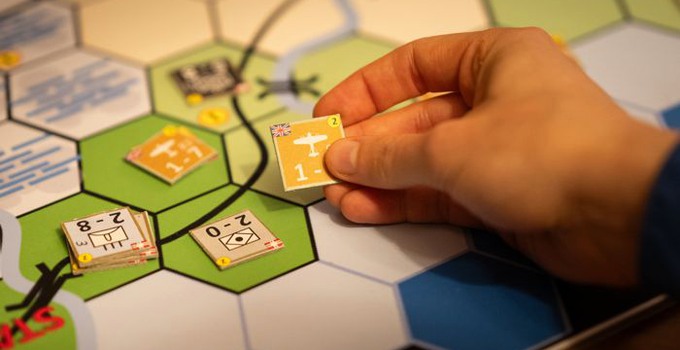 Hand som håller i en spelbricka över ett brädspel.