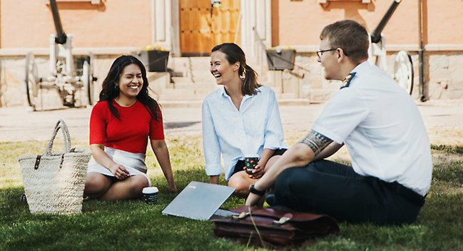 Två studenter och en officersstuderande sitter framför Försvarshögskolans entré vid den gamla byggnaden.